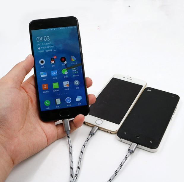 Hand holding a smartphone connected to two other phones with a three-in-one USB charging cable.